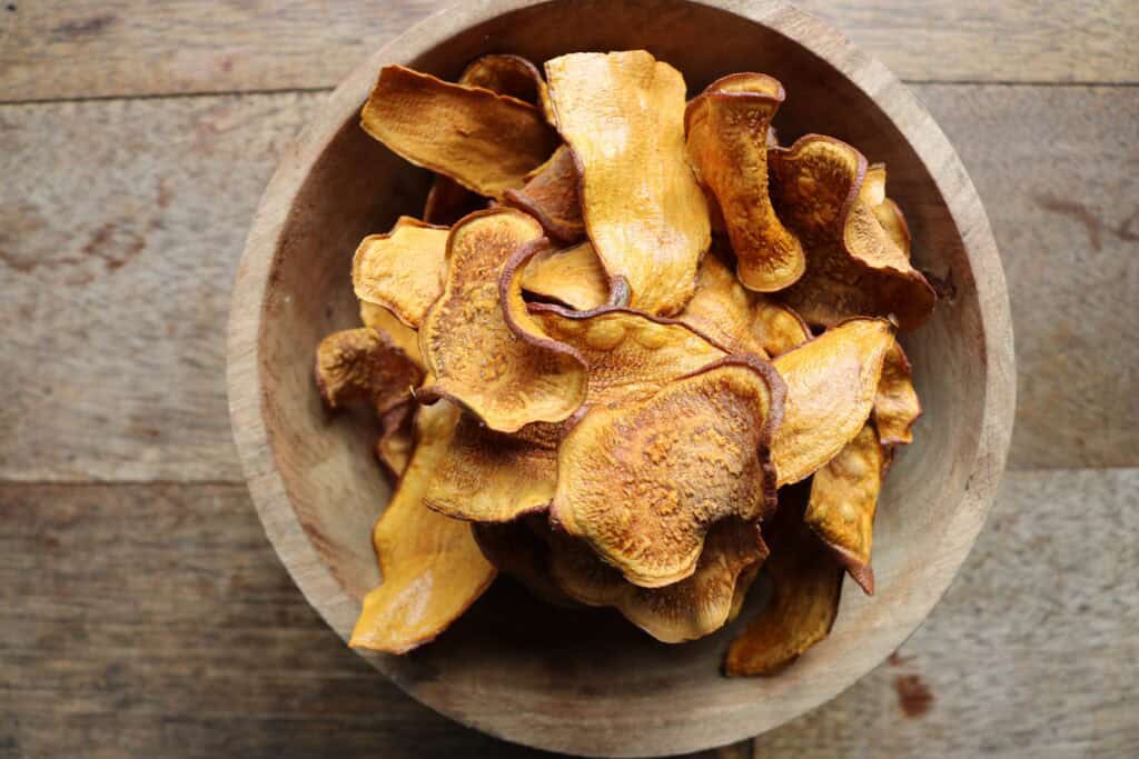 chips van zoete aardappel in houten kom op houten tafel. Groentechips.
