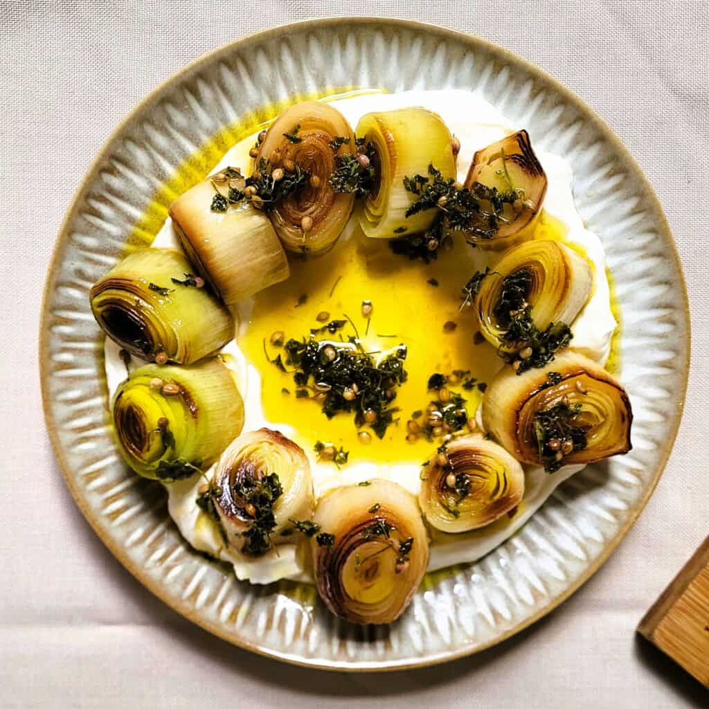 Labneh met kruiden, olijfolie en gegrilde uien op een bord.