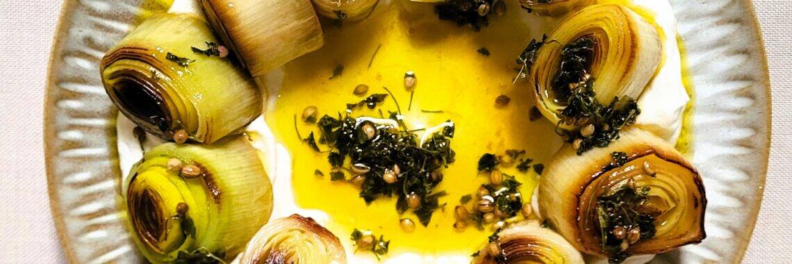 Labneh met kruiden, olijfolie en gegrilde uien op een bord.