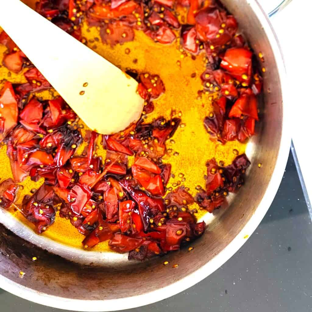 Gekonfijte paprika in een pan met olie en kruiden. Perfect als smaakmaker of bijgerecht.